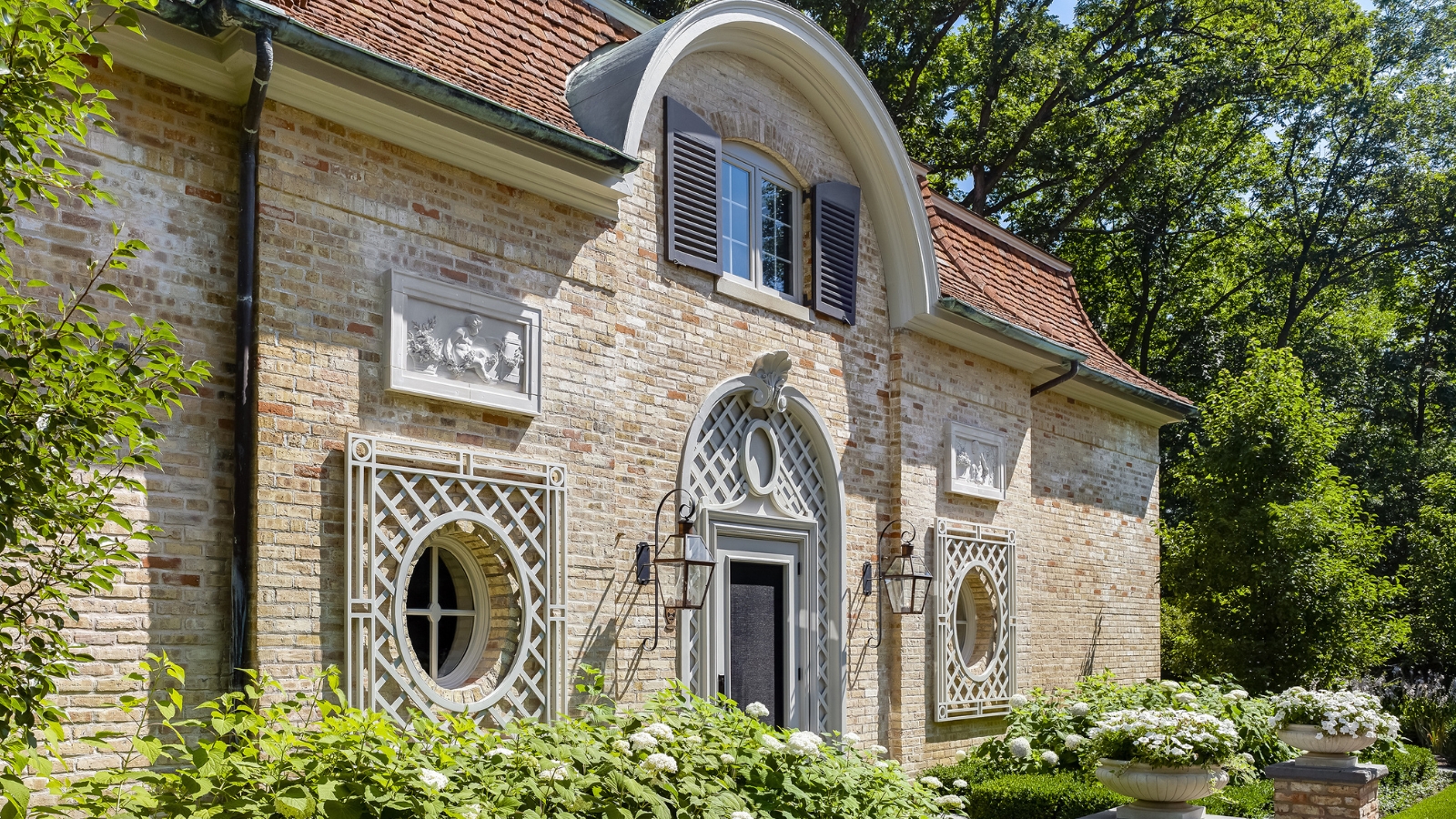 Historic building with brick exterior, round windows and detailed archway, surrounded by trees and greenery