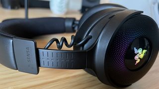 Razer Kraken V4 Pro on its side with one headband slider up to max, showing extension of coiled cable running to the cup