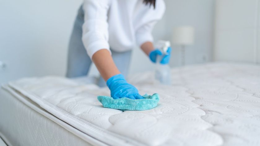 A hand holding a cloth scrubbing the surface of a mattress with the other hand holding a spray bottle