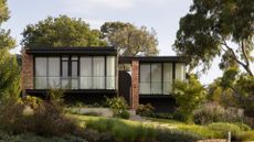 A beautiful big house with a black and red brick facade and a lush garden with ground cover and trees