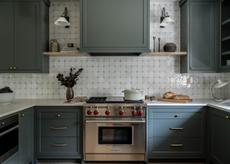 A muted dark blue symmetrical kitchen with wall lights and a centrepiece focal point of a stainless steel cooker