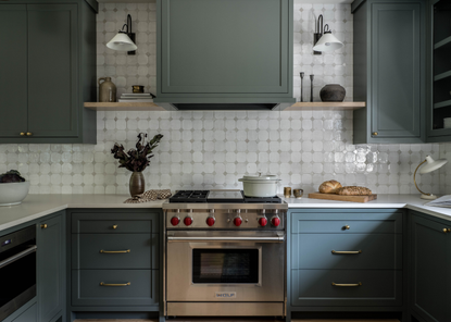 A muted dark blue symmetrical kitchen with wall lights and a centrepiece focal point of a stainless steel cooker