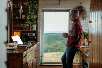 A pensive older man is at home drinking coffee and relaxing in his beautiful kitchen at home.