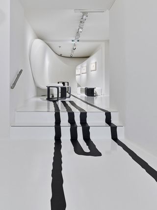Galerie Gmurzynska Gallery. The room is all white, with black lines on the floor. In the distance, we see a few black marble tables.