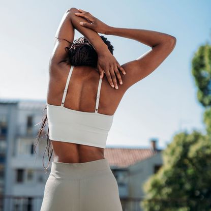 A woman doing some of the best exercises for back pain, stretching her hand behind her back