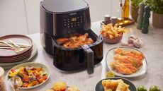 A Philips air fryer with an open draw full of food, surrounded by plates of food