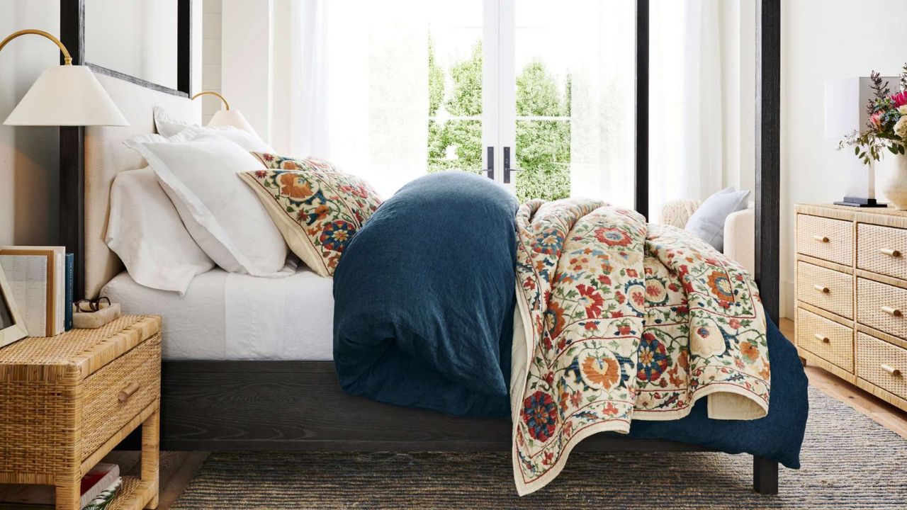 Rustic bedroom with four-poster black bed, blue bedding with patterned throw and pillows, wicker furniture and gray rug