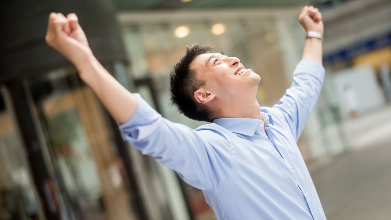 An investor celebrates with his hands in the air.