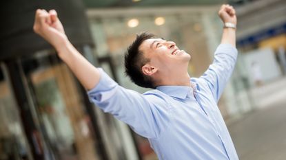 An investor celebrates with his hands in the air.