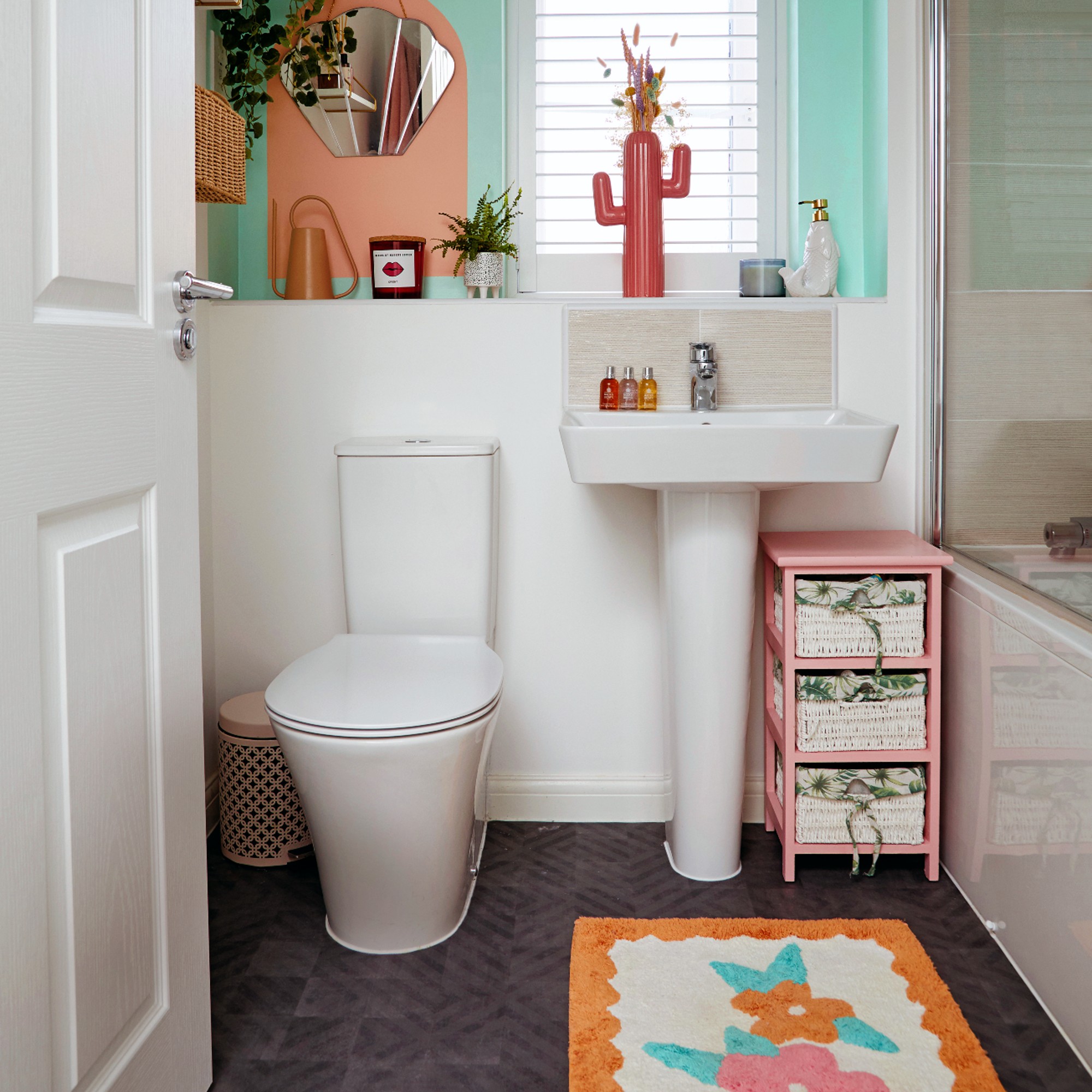 White bathroom with toilet, sink, bath and decorated with colourful bath mat
