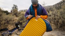 Airbeds vs camp beds vs sleep mats: man blowing up a yellow Thermarest camping pad outdoors