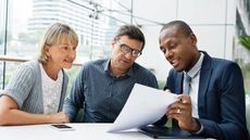 An adviser holds up a sheet of paper and explains its contents to an older couple