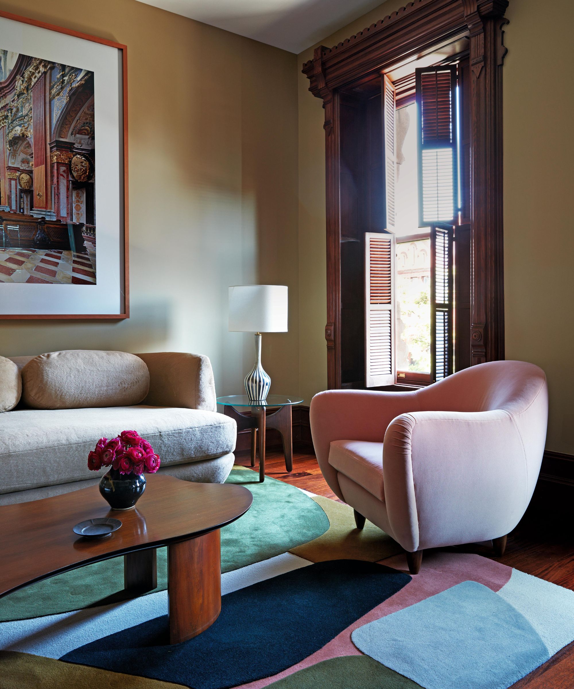 a neutral living room in a new york apartment with original large mahogany sash windows and modern colorful curved decor
