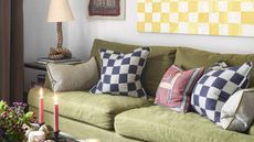 Sitting room with a green sofa and checked cushions, a yellow and white checked wall hanging and candles lit on a table. 