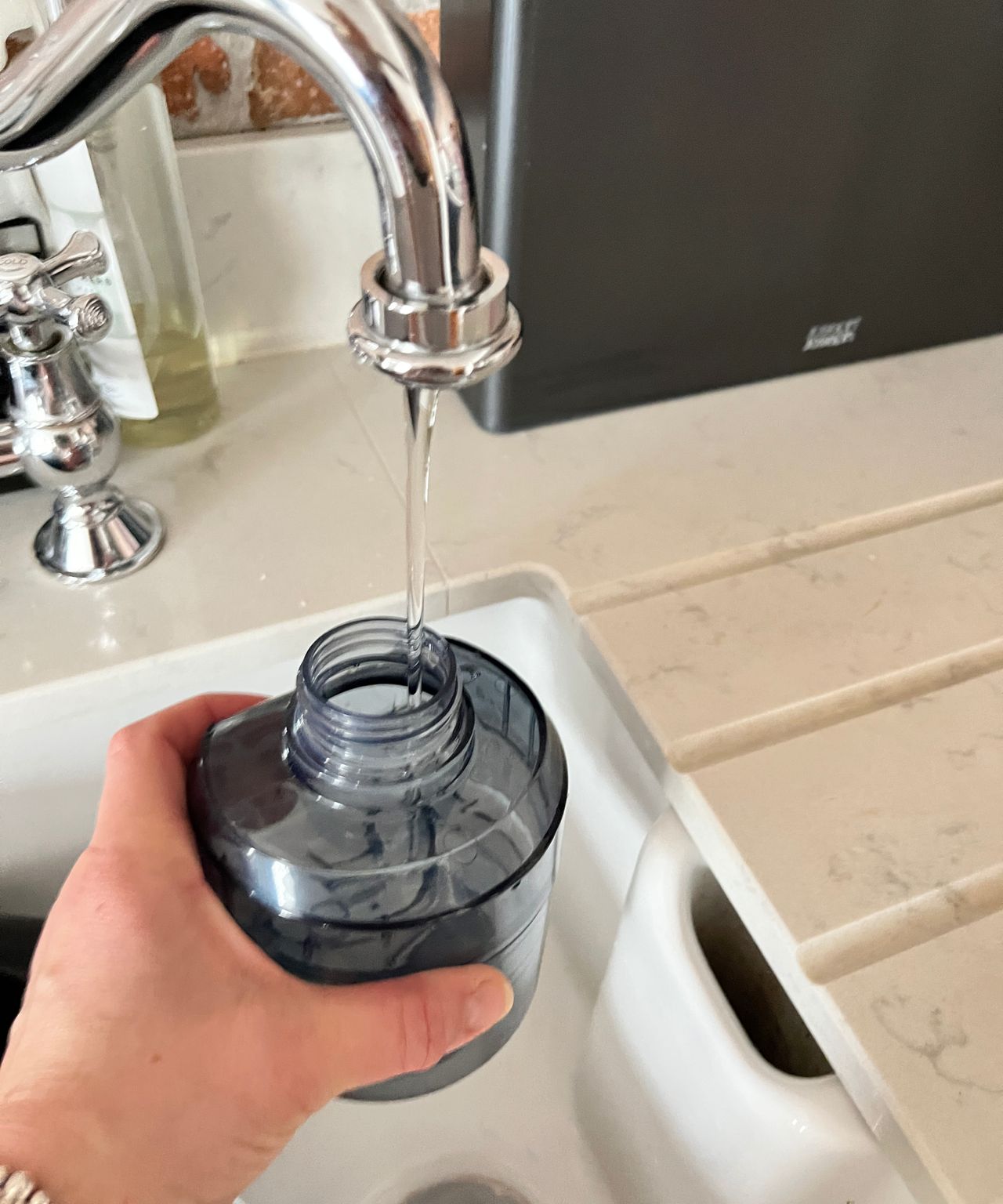 hand holding water dispenser being filled from chrome swan-necked tap