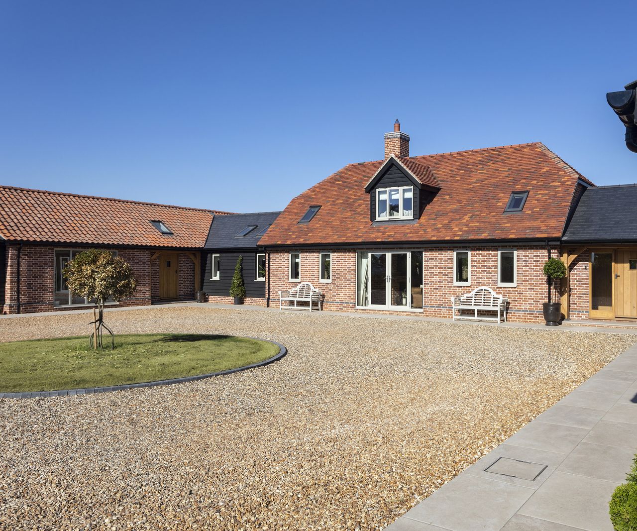 An angled view of a barn-style new home with a large gravel driveway out front