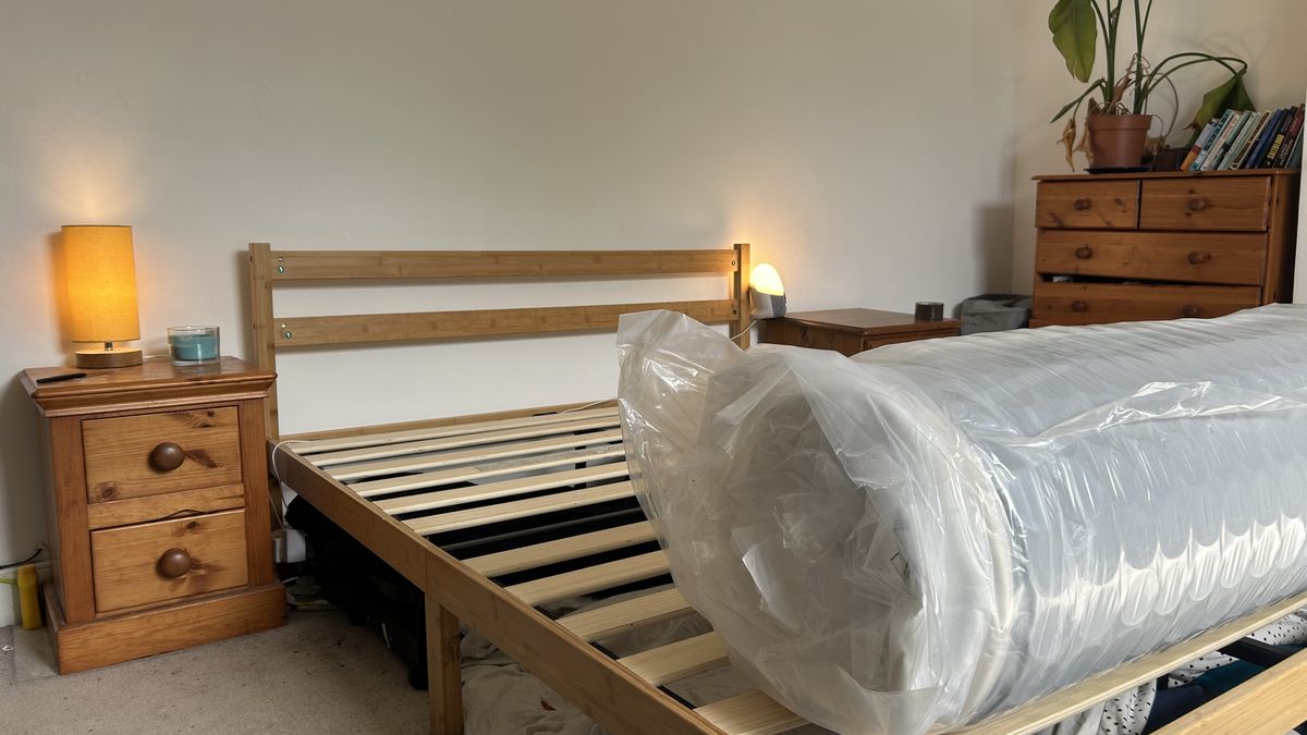 A rolled up Awara Classic mattress on a wooden bed frame