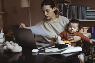 mum holding baby and a looking at a bill in front of her laptop