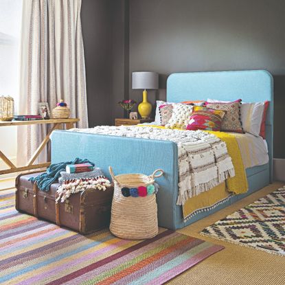 A bedroom with a sky blue bed frame and two patterned rugs layered on top of a neutral-coloured carpet