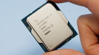 An Intel Core i9 14900K CPU held by a person, using a finger and a thumb, against a pale blue background