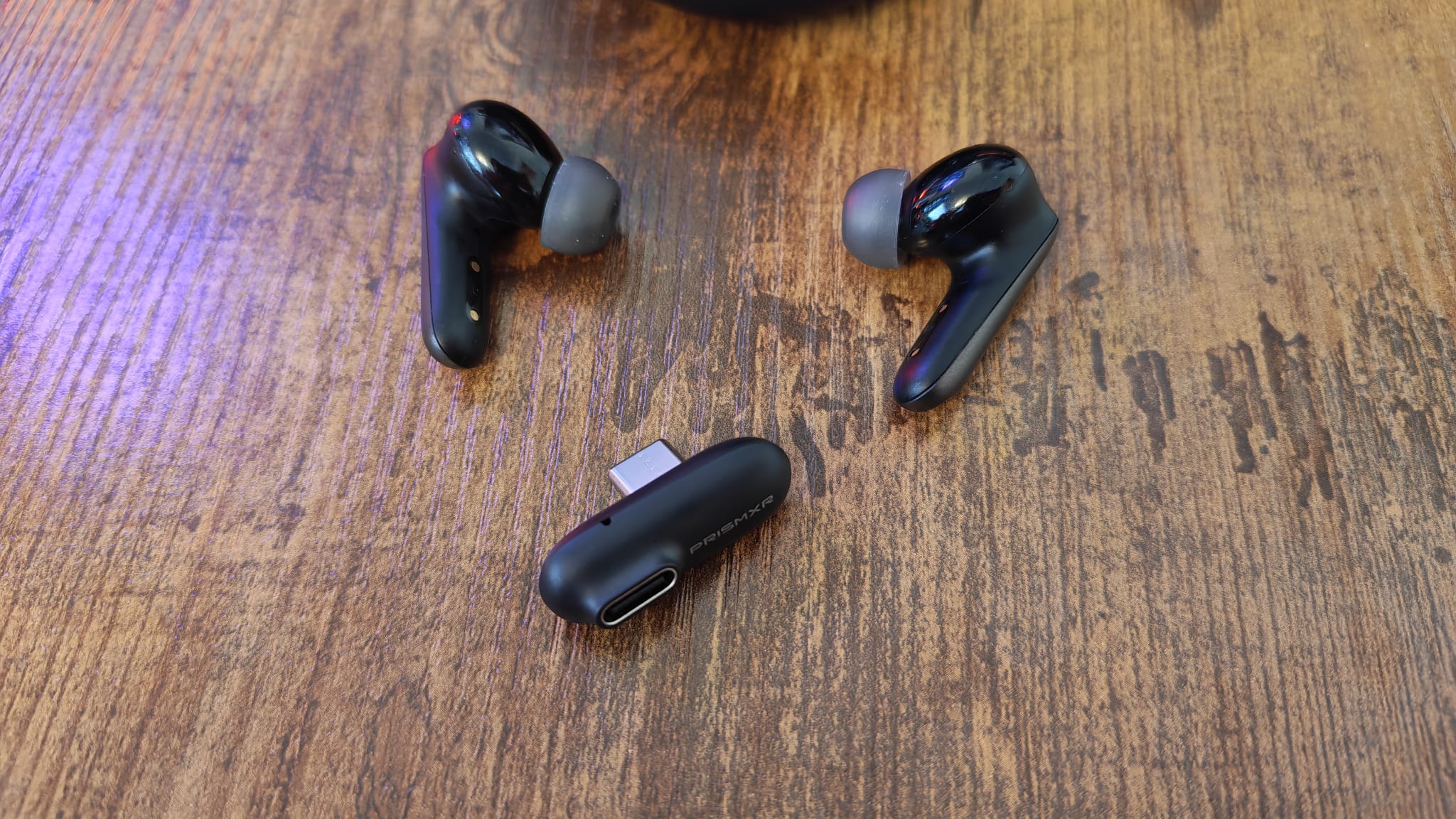 The PrismXR Vega T1 earbuds lying on a wooden desk next to their USB dongle