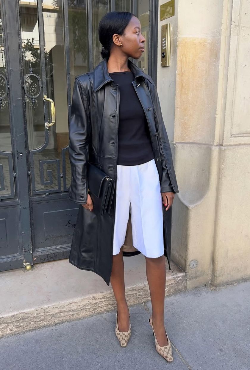 @sylviemus_ wears a long black leather coat, black top, white long shorts, a brown printed pumps
