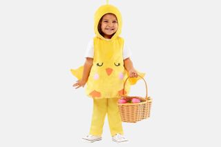 A smiling child wears a cute Easter chick costume and holds a basket ready for an easter egg hunt