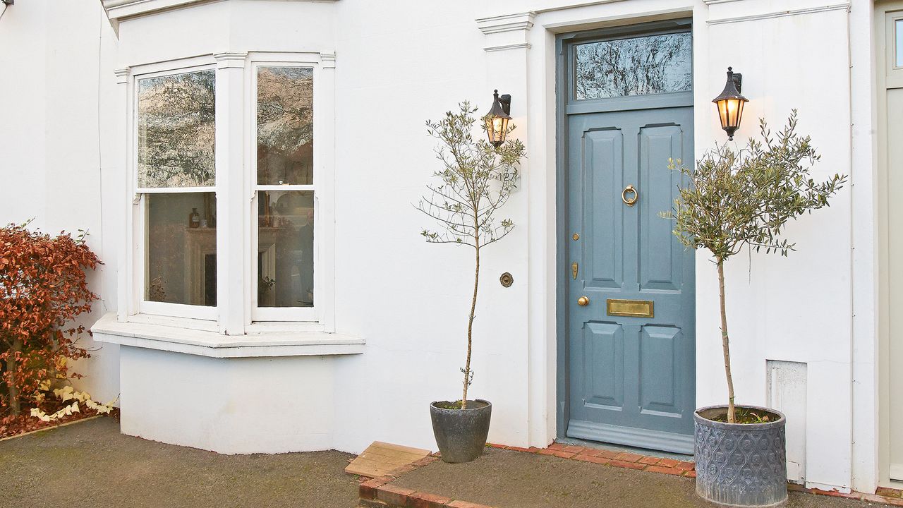 white house exterior with blue front door, wall lights and plants