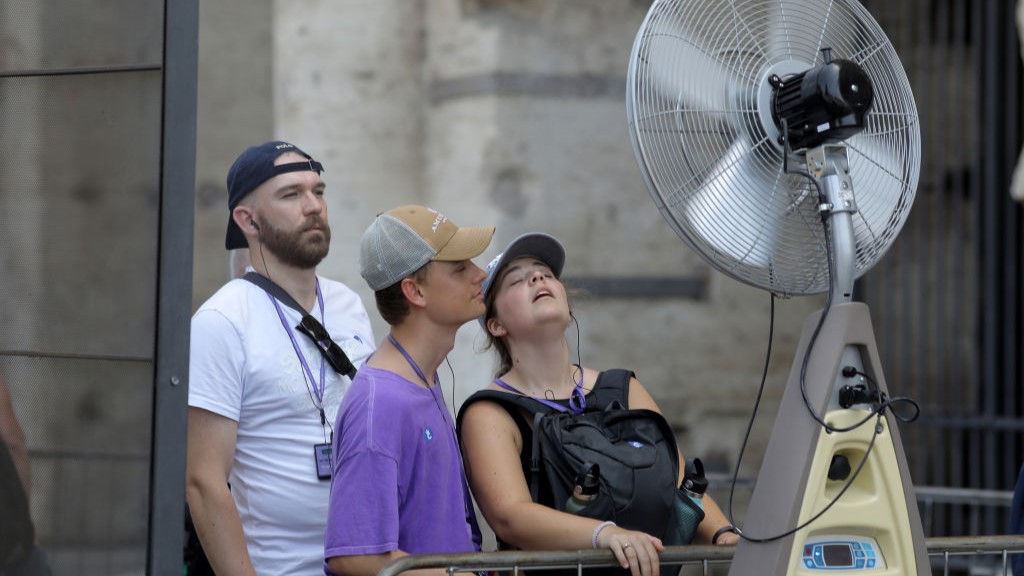 Three tourists stand close to a fan spraying nebulized water during summer 2023 in Rome, Italy.