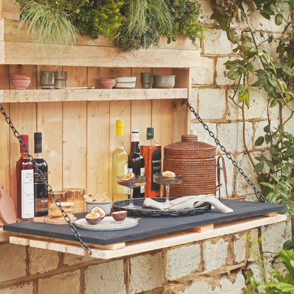 A fold down bar attached to the stone wall with a shelf and storage. Rattan ice bucket and passion fruit martini.