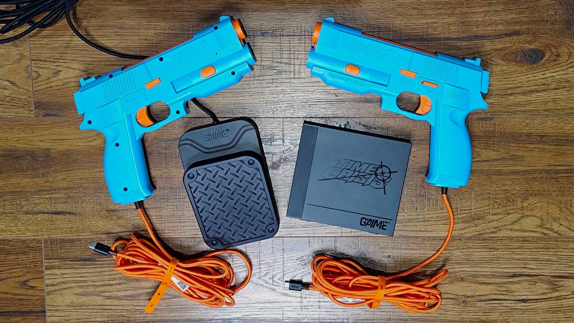 G&#039;AIM&#039;E Time Crisis Lightgun Console on wood floor with two lightguns at top and base box and pedal in middle.