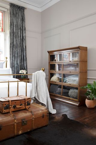 Bedroom with bed with white bed linen, two trunks at the foot, vintage storage and dark wood floor