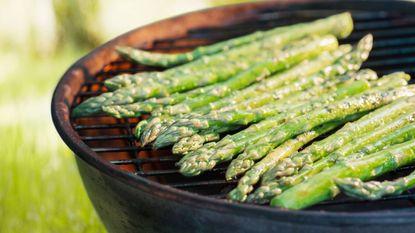 A close up shot of spears of asparagus cooking on a charcoal grill