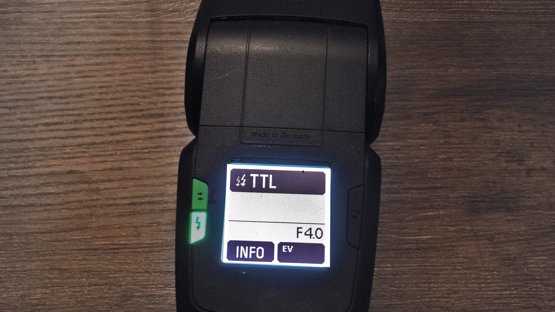 Close-up of a camera flash unit display showing TTL mode and F4.0 settings, placed on a wooden surface