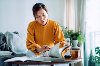 Focused young woman reading book and making notes at home, concentrates on her studies. Further education concept