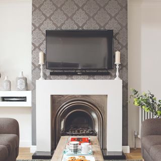 A living room with a feature wall covered in wallpaper with a TV placed above the fireplace