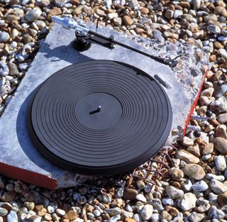 Concrete Stereo, 1983. A broken record player lying on gravel.