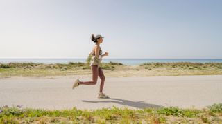 Woman running along pathway with sea and greenery in the background