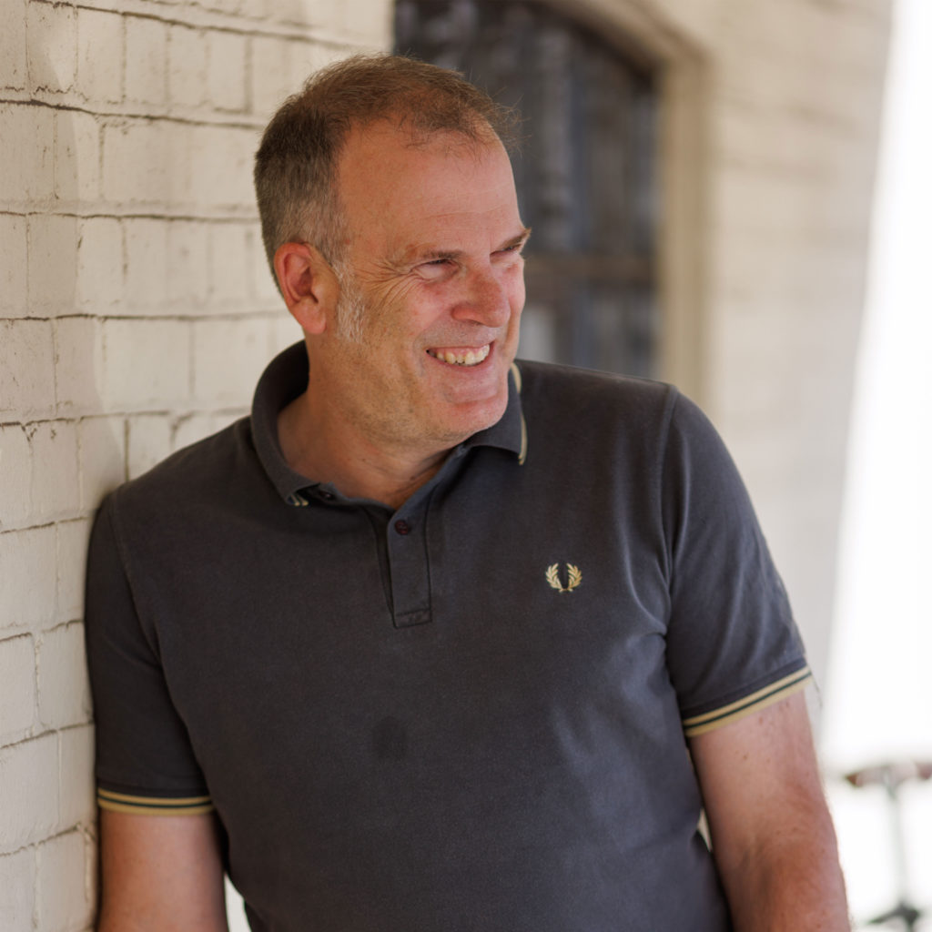 male leaning against light brick wall wearing navy short sleeved polo shirt