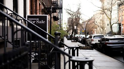 A for sale sign in front of a townhouse on a city street.