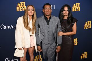 Jennifer Lopez holds a Strathberry bag and wears a white oversized jacket and pink bubble skirt as she poses with Anthony Robles and Judy Robles at AFI FEST 2024