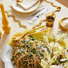 Dining room tablescape with lemon yellow tablecloth and large plate of pasta.