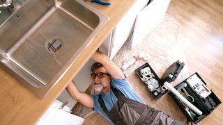 Man in overalls lying under kitchen sink and fitting water supply to taps