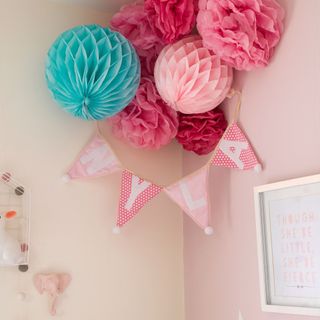 Corner of a pink nursery, with colourful paper decorations tied in a cluster