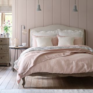 bedroom with pink striped wall wooden floor and bed with pink and white cushion