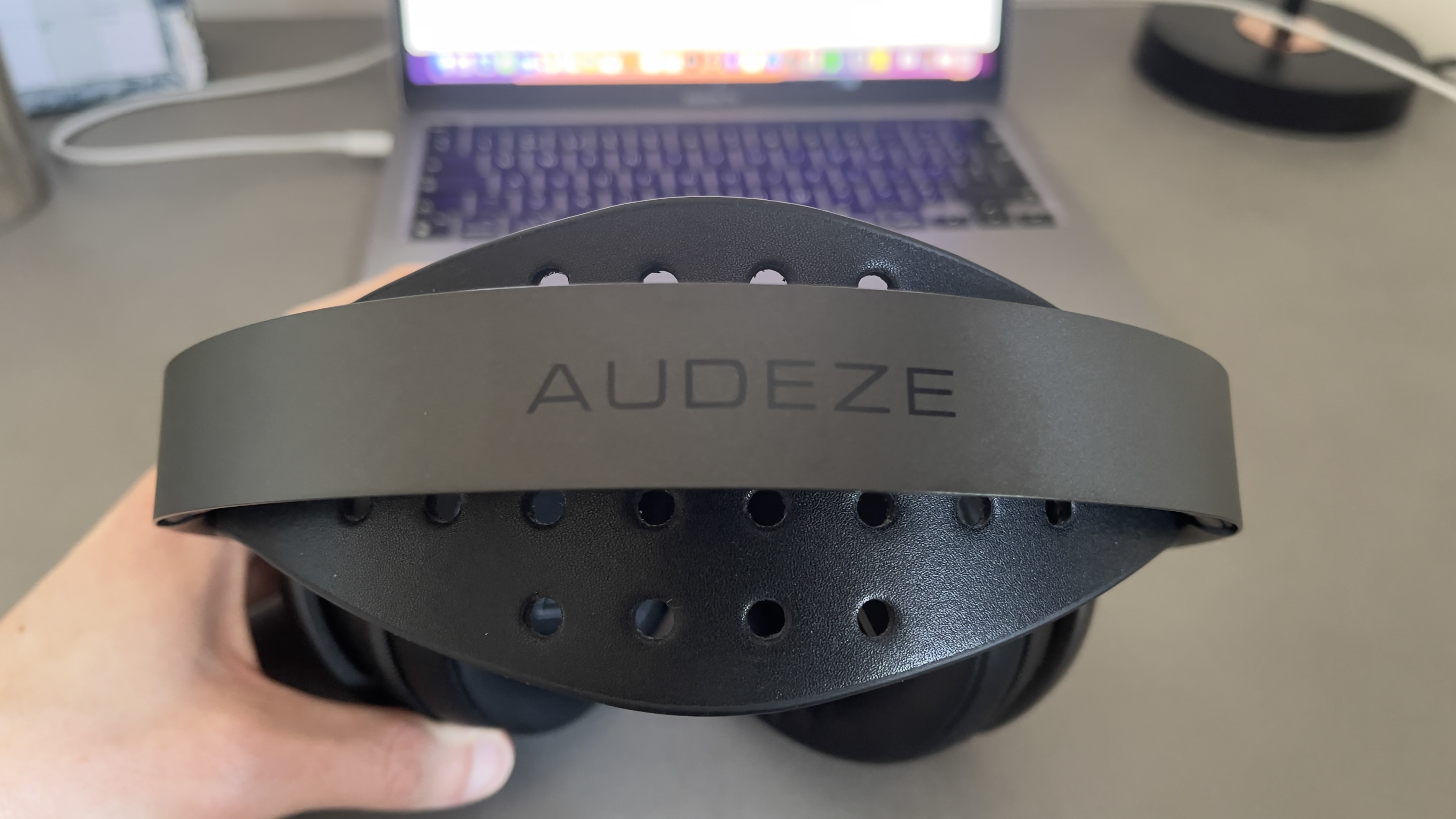 The Audeze Maxwell 2 gaming headset lying on a pale desk with the top pointing toward the camera and being held in a hand