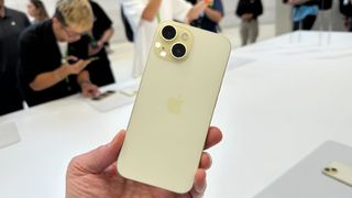 The back of a yellow iPhone 15 being held by the hand of TechRadar's Lance Ulanoff. It's been picked up off a white table.