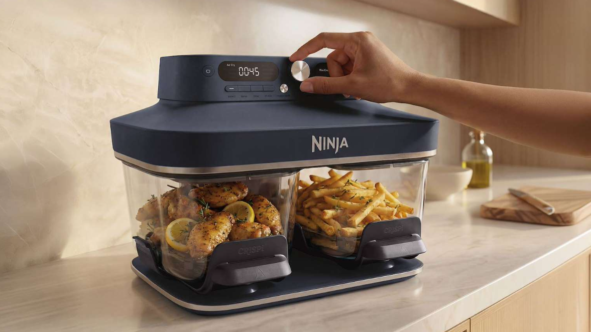 Ninja Crispi DualZone Air Fryer with food inside and person's hand using control dial