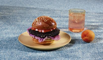 A black chicken burger sits on a table with a blue cloth