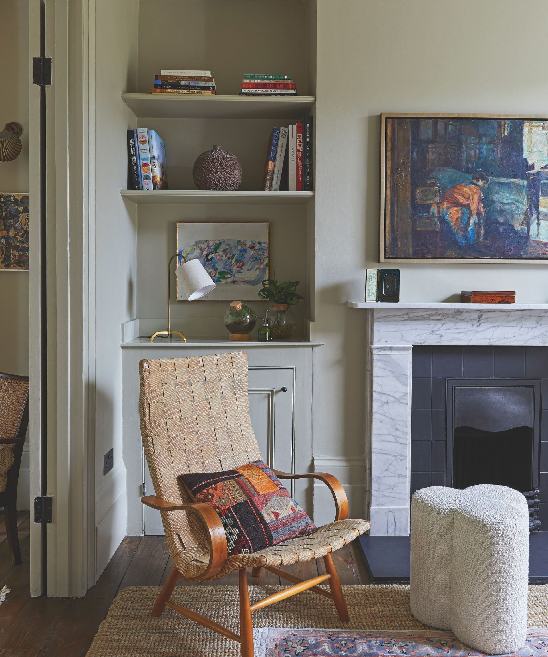 Living room with open shelving, marble fireplace and painting and woven armchair with boucle stool beside it